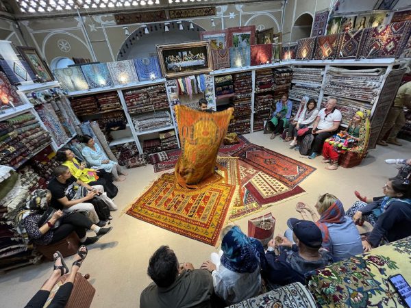 Tourists browsing colorful Persian carpets in a Yazd bazaar carpet shop | Iran&rsquo;s Travel