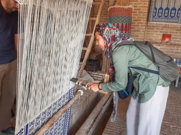 A smiling tourist waving inside the Ziloo Museum in Meybod, surrounded by traditional Persian looms and woven rugs | Iran&rsquo;s Travel